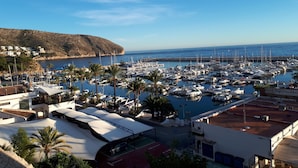 Una marina con numerosos barcos amarrados, un pueblo costero al fondo y un edificio destacado con un letrero que dice 'Roof Top Cocktails'.