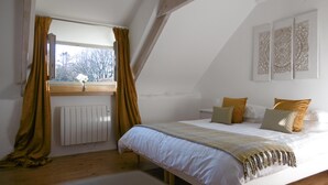 Ein Schlafzimmer mit einem großen Bett, einem Fenster mit Vorhängen, einem Heizkörper und dekorativen Wandverkleidungen.