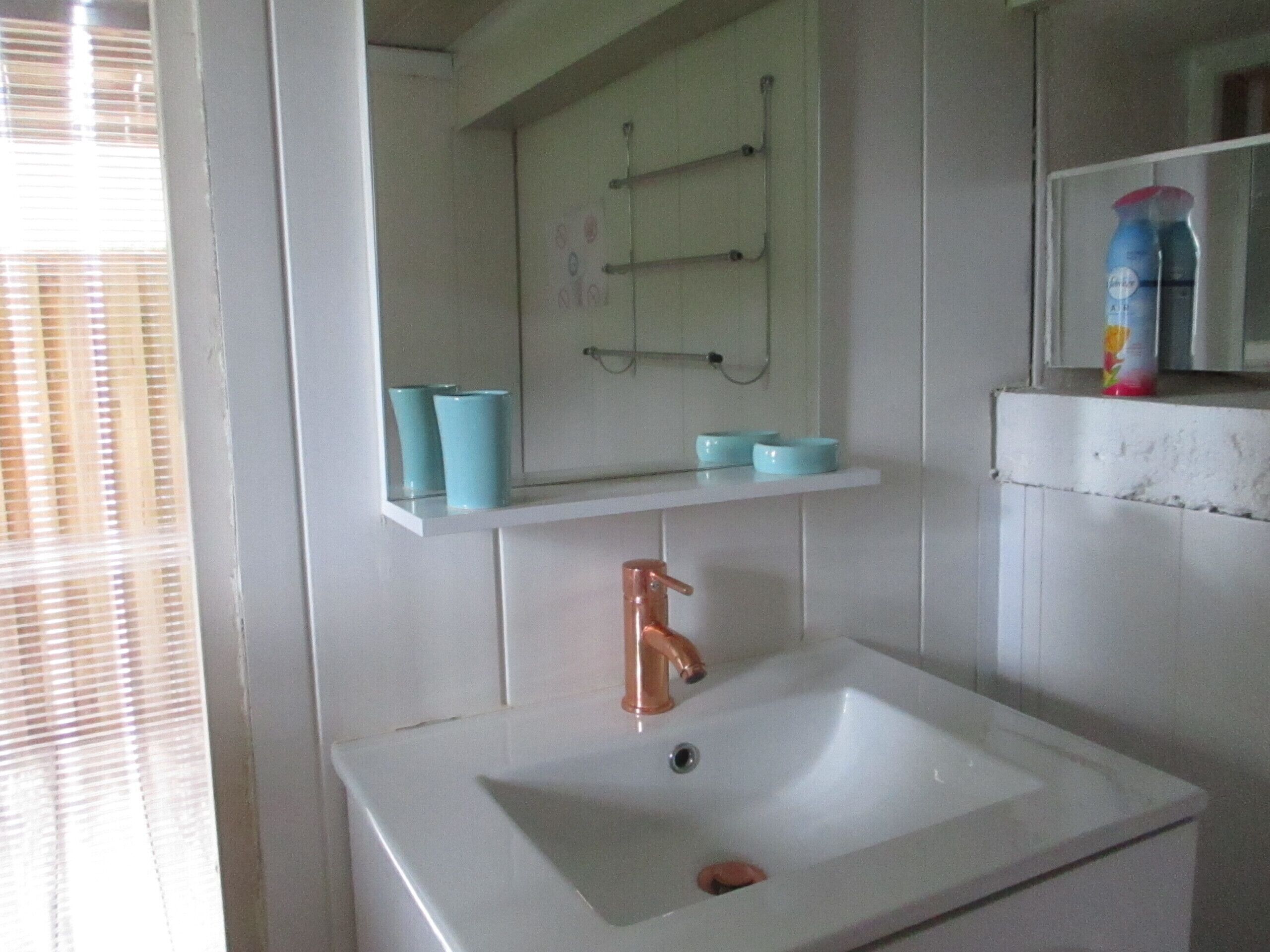 Un bany amb un lavabo blanc, un mirall i una petxina amb gots blaus.