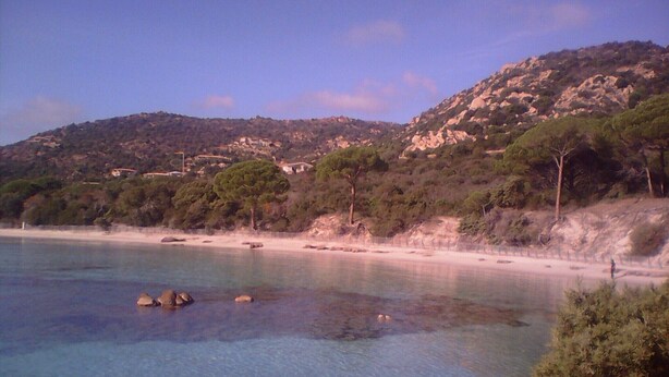 A coastal landscape with clear water, rocky shore, and a hilly backdrop. - U vene e posa - the Pinzelli mountain.  (Lugo-Di-Nazza)