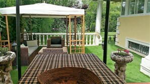 A covered patio with a checkered floor, a wooden pergola, and a garden view.