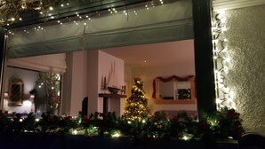 A room with a Christmas tree decorated with lights and ornaments, a fireplace, and a mirror with a garland.