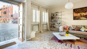 Een ruime woonkamer met een groot raam, een bank, een salontafel en een boekenkast.