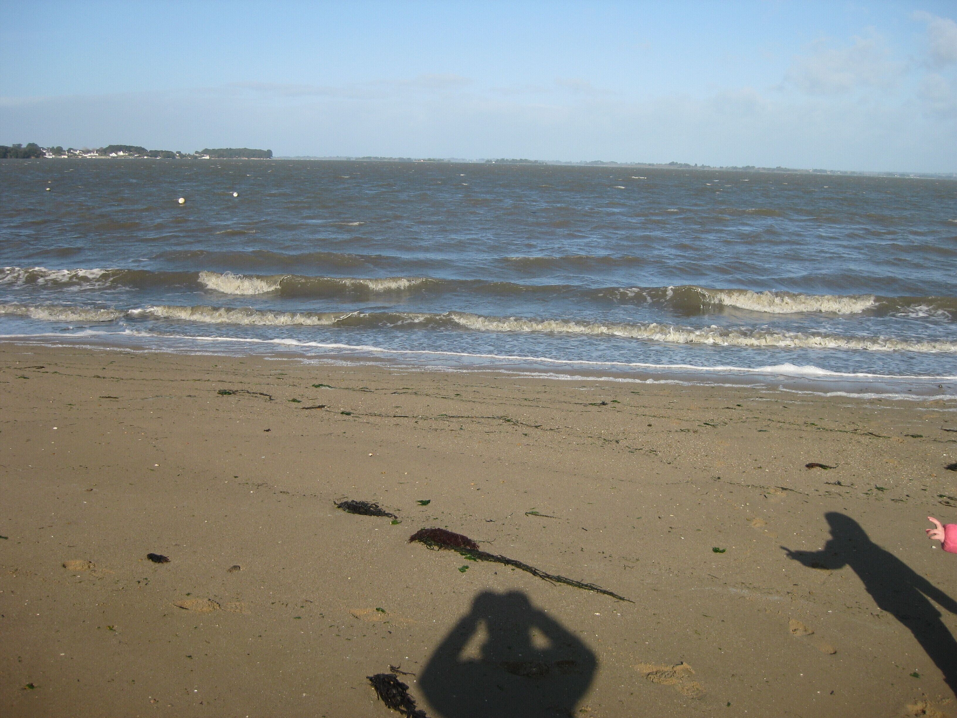 Une plage avec des vagues et l’ombre d’une personne.