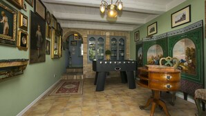 A room with a billiards table, a wooden chest of drawers, and a green wall with framed pictures.
