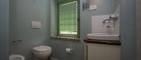 A bathroom with a toilet, bidet, sink, and a window with blinds.