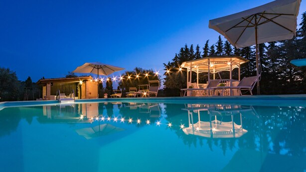 A swimming pool with lounge chairs and umbrellas, surrounded by trees and a gazebo.