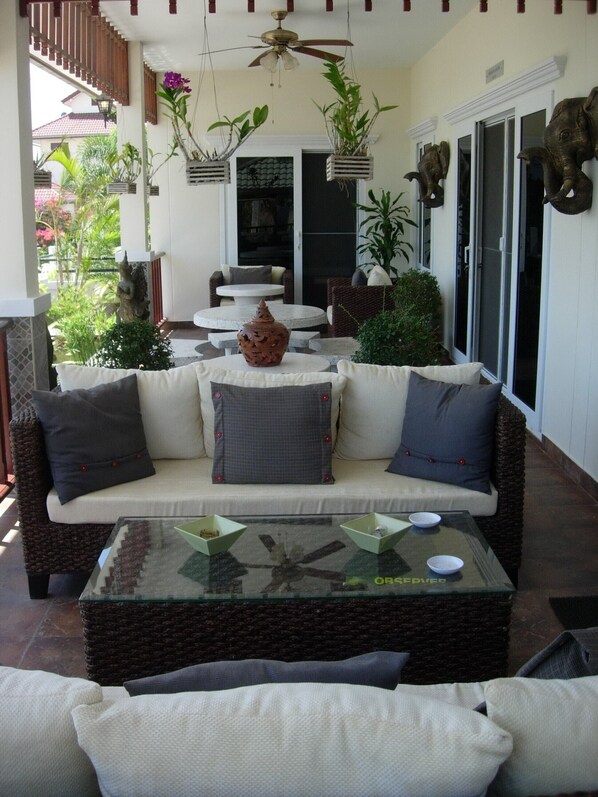 Un patio soleado con mobiliario de mimbre, una mesa de centro de vidrio y plantas decorativas.