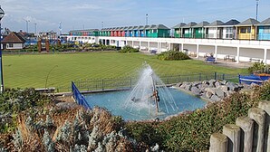 A swimming pool with a fountain, surrounded by a fence and greenery.