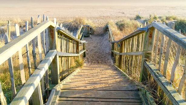 A wooden staircase leading to a beach with a wooden railing on both sides.