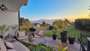 Une terrasse avec des meubles en osier, une table en verre et des plantes en pot.