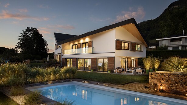 Une maison moderne à deux étages, dotée d’une piscine, entourée d’un jardin aménagé et offrant une vue sur les montagnes.