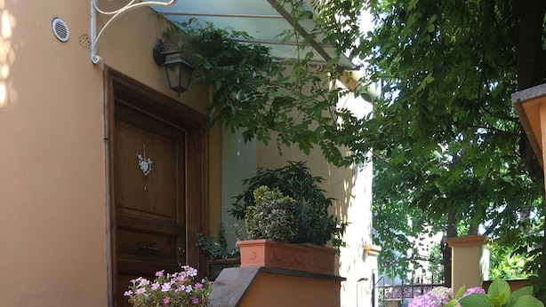 L’entrée d’un immeuble, avec une porte en bois, des marches menant à cette porte et un pot de fleurs contenant des plantes aux fleurs roses.