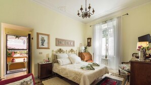 Une chambre bien éclairée, avec un lit, des tables de chevet, une commode, un lustre et une fenêtre avec des rideaux.