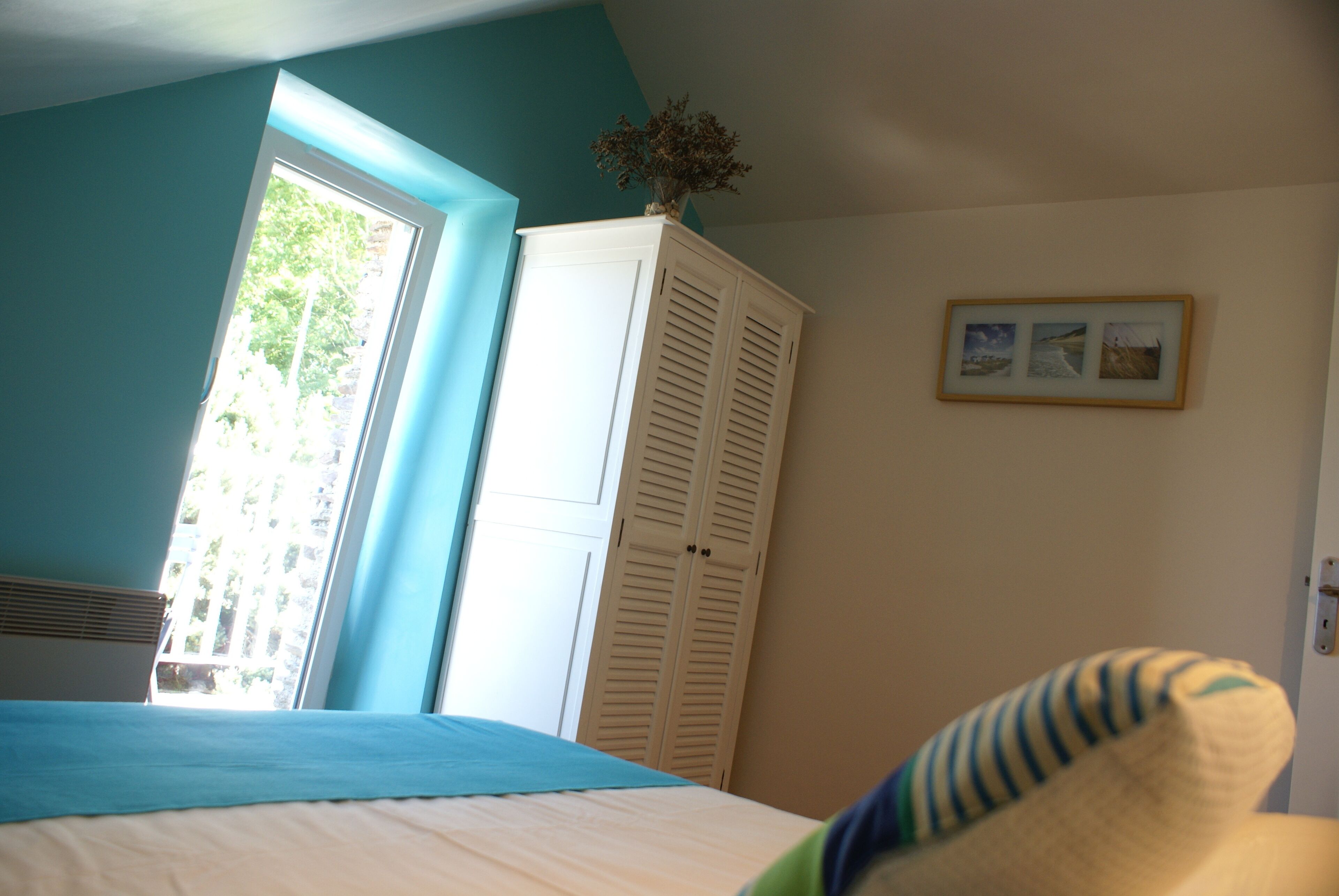 Une chambre à coucher avec un lit, une armoire, une fenêtre et un tableau encadré au mur.