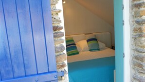 Ein Schlafzimmer mit Steinsandsteinwand, einer blauen Tür und einem Bett mit gestreiften Kissen.