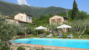 A swimming pool with lounge chairs and umbrellas, surrounded by houses and mountains. - Torretta - Luxury rustico with pool and air conditioning EV wallbox (Camaiore)