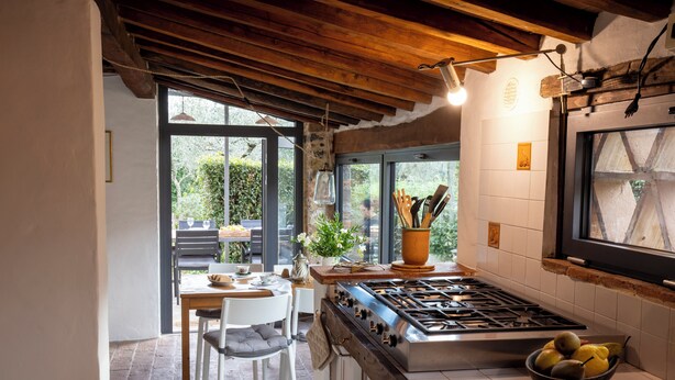 A kitchen with a gas stove, a dining table with chairs, and a window overlooking a garden. - Torretta - Luxury rustico with pool and air conditioning EV wallbox (Camaiore)
