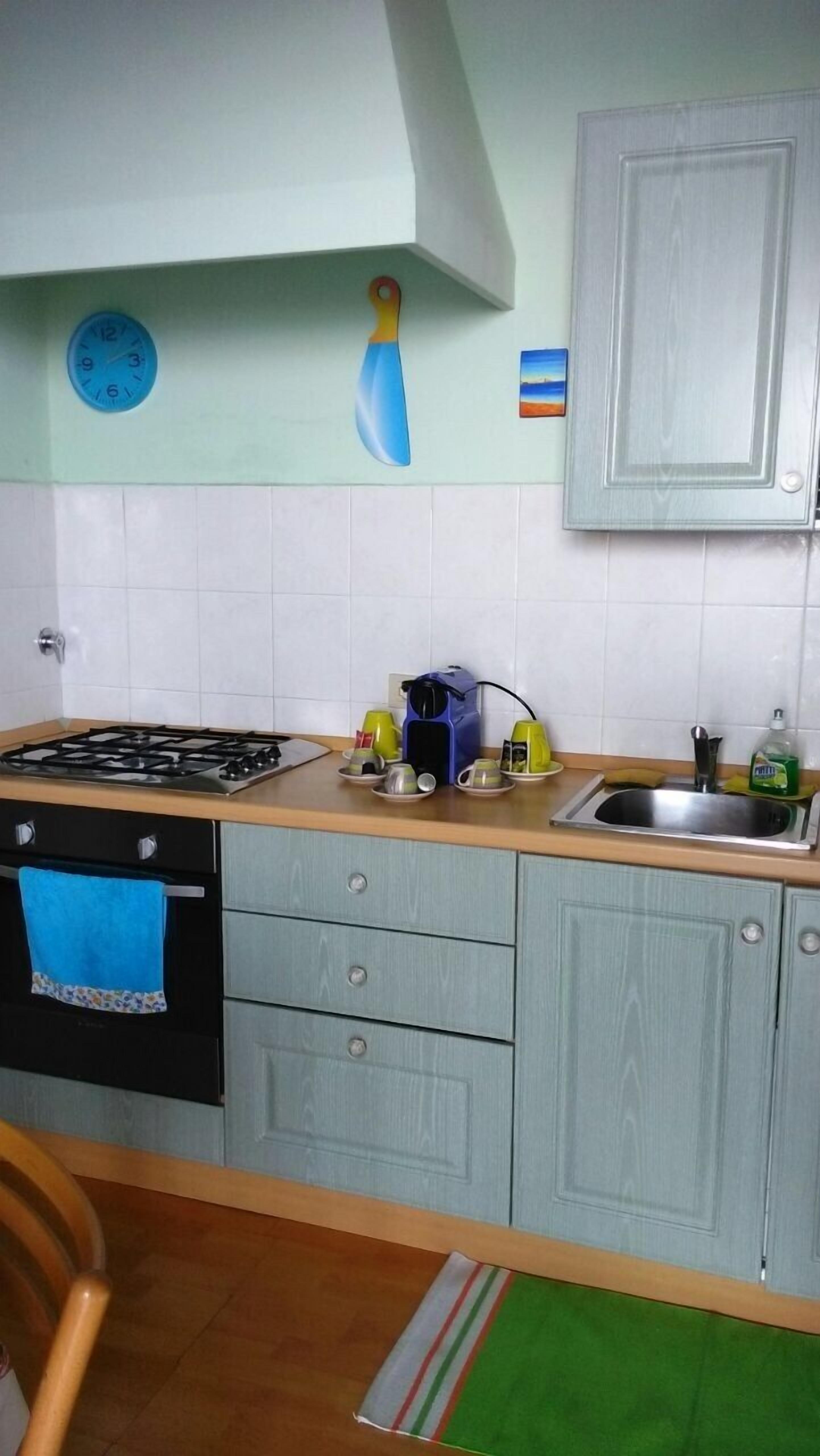 A kitchen with a gas stove, a sink, cabinets, a clock, and a painting on the wall.