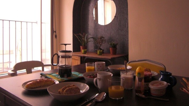 A breakfast table with various dishes and drinks, a coffee maker, and a view of the outside balcony. - Unique Space in the Heart of La Bastide (Carcassonne)