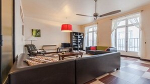 A living room with a sofa, a coffee table, a TV, a bookshelf, and a ceiling fan. - Unique Space in the Heart of La Bastide (Carcassonne)