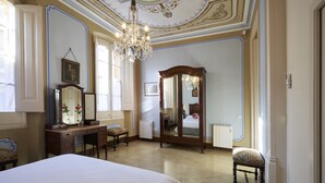Une chambre spacieuse avec un grand lit, une commode en bois, une coiffeuse avec un miroir et un lustre.
