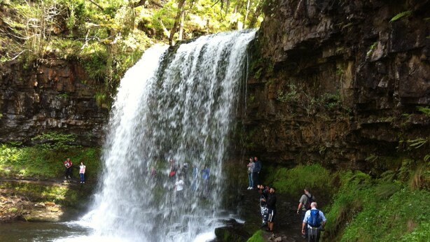A waterfall cascading down a rocky cliff into a pool, surrounded by lush greenery and a few hikers on a trail. - "266" 4 STAR!  HOT-TUB, LOG-FIRE, BQ, PLAYGROUND, BIKE LOCKUP, Nr Zip World  (Aberdare)