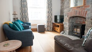 A cozy living room with a blue sofa, a brown leather couch, a small round table, a TV on a wooden stand, and a stone fireplace.