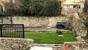 A stone staircase leading down to a grassy area with a stone wall and a metal gate.