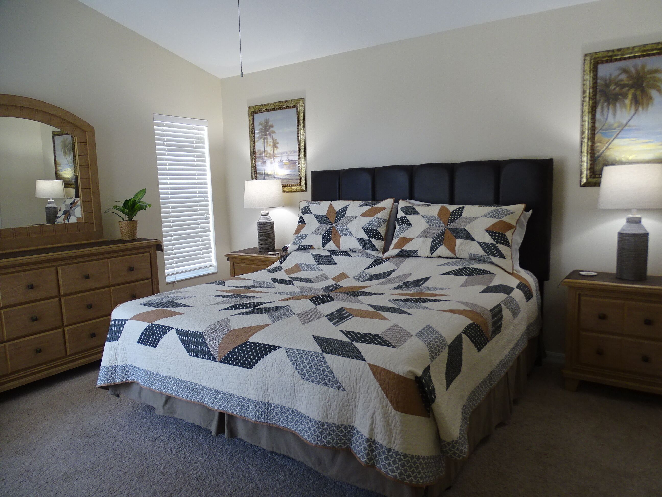 Une chambre à coucher comprenant un lit, deux tables de chevet, une commode, une fenêtre avec des stores et un miroir fixé au mur.