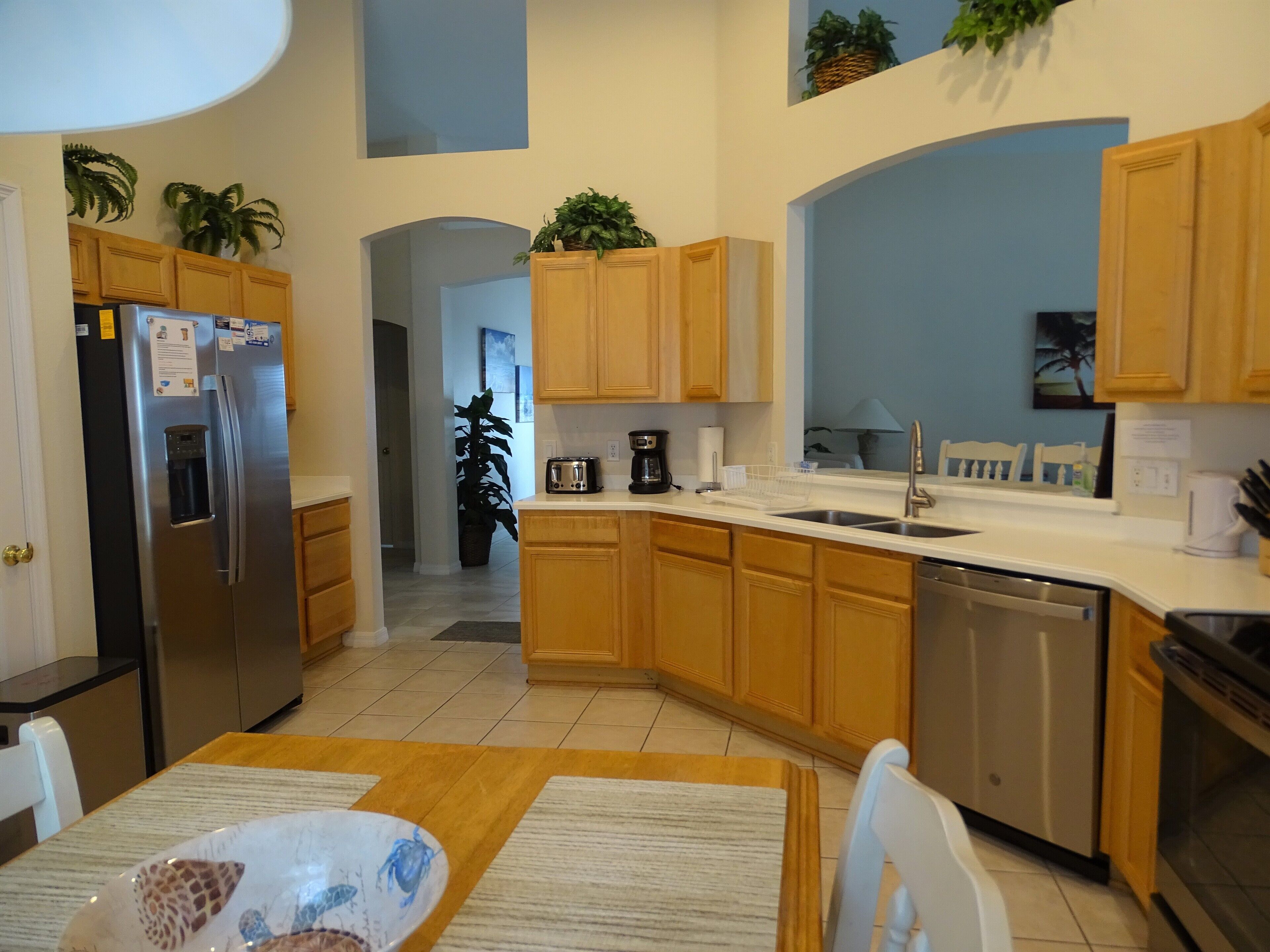 Una cocina moderna con armarios de madera, un refrigerador de acero inoxidable, un lavavajillas y un comedor con mesa y sillas.