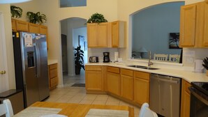 A modern kitchen with wooden cabinets, a stainless steel refrigerator, a dishwasher, and a dining area with a table and chairs. -  Stylish Ever Popular House with Large Solar Heated Pool/Spa in Gated Community  (Davenport)
