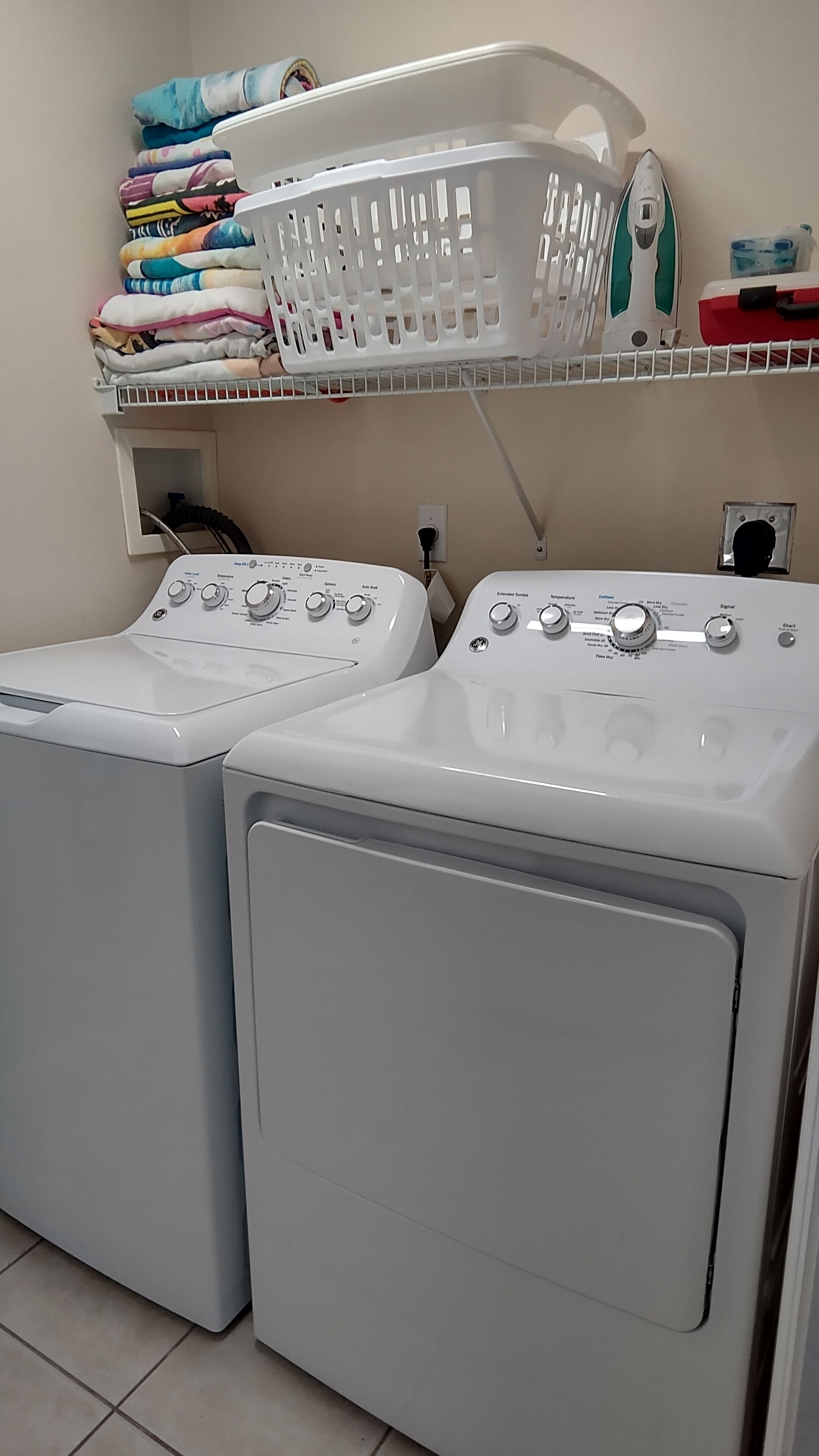 A laundry area with two front-loading washing machines and a stacked laundry basket on a shelf above.