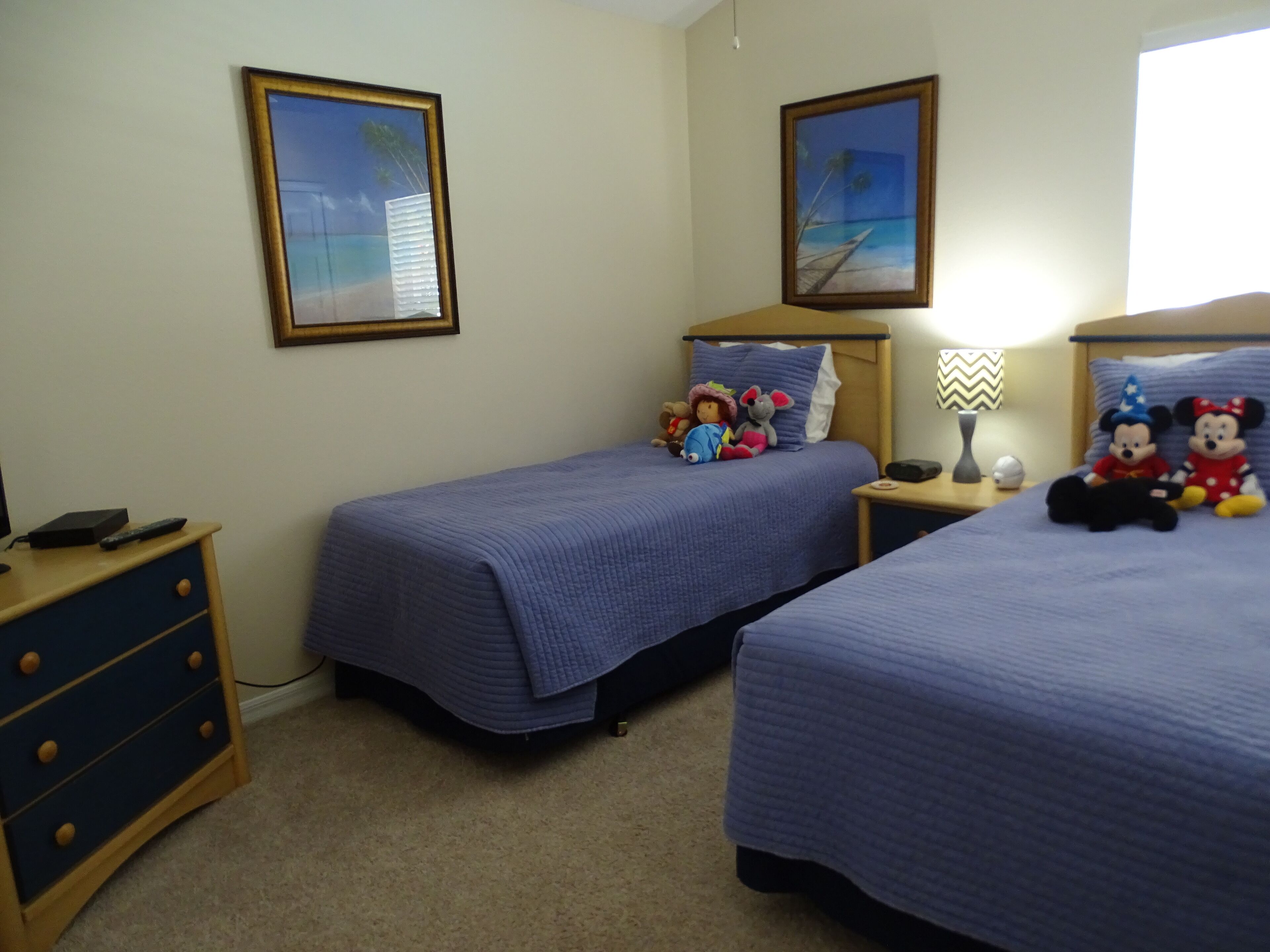 Une chambre avec deux lits, une table de chevet, une commode et deux tableaux encadrés accrochés au mur.