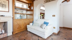 A white sofa with blue and beige cushions, a wooden cabinet with glass doors, and a fireplace.
