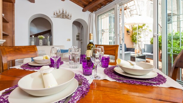 A dining table set with white plates, purple napkins, and clear glasses.