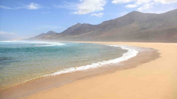 Une plage aux eaux cristallines, avec des montagnes qui se dessinent à l’horizon.