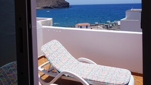 Un balcon avec deux fauteuils blancs et une vue sur la mer et une île rocheuse.