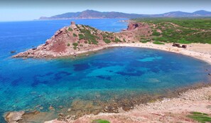 Paisagem costeira com mar azul límpido, uma península rochosa e uma área de praia.