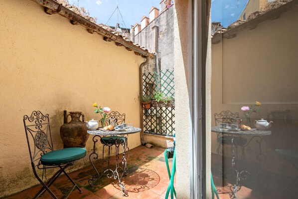 A small outdoor patio with a table and chairs, a large vase, and a potted plant.