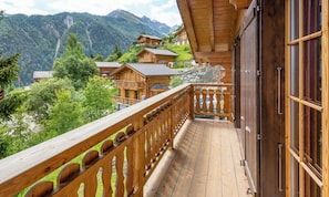 Un balcon en bois offrant une vue sur un paysage montagneux et sur d’autres bâtiments.