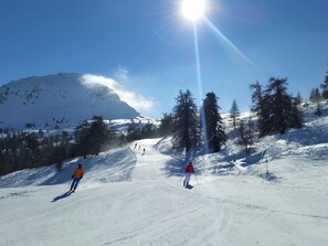 Une piste de ski enneigée avec des skieurs, une montagne en arrière-plan et un ciel dégagé.