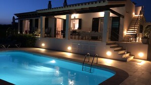 Un área moderna junto a la piscina con una zona de estar cubierta, una piscina y una escalera que lleva a un nivel superior.