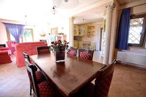 A dining area with a wooden table and chairs, a vase of flowers, and a view of a kitchen and living room through an open door. - Exclusive villa very close to the station for Rome and Pompei ! (Genzano di Roma)