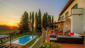 A poolside area with a sunken seating arrangement, a wooden deck, and a view of the sunset. -  "Villa Torre in Chianti"  Vrbo Vacation Rental of the Year 2026- 8 bedrooms A/C (San Casciano in Val di Pesa)