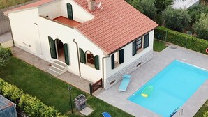 Une maison à deux étages avec une piscine, un patio doté d’une chaise longue et un petit jardin.