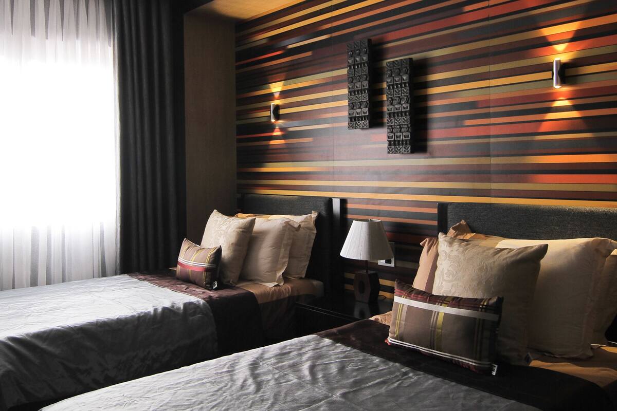 Une chambre d’hôtel avec deux lits, une table de chevet, une lampe et un mur orné d’un motif à rayures.
