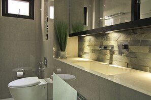 A modern bathroom with a stone backsplash, a toilet, a sink, and a mirror.