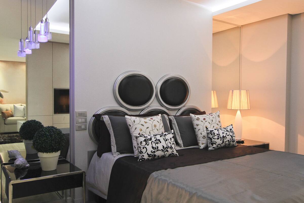 Une chambre moderne avec un grand lit, une table de chevet avec une lampe et un miroir fixé au mur.
