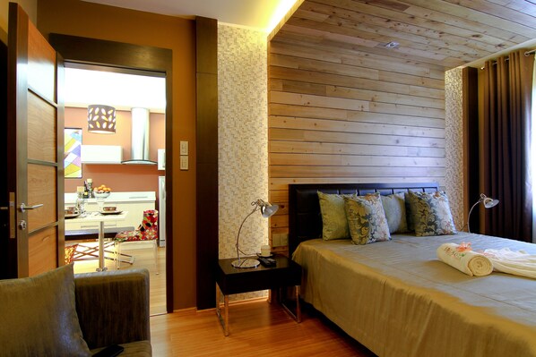 A hotel room with a wooden ceiling, a bed with a beige bedspread, a nightstand with a lamp, and a chair.